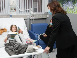 Dame Rachel de Souza speaking to a child patient in a hospital bed